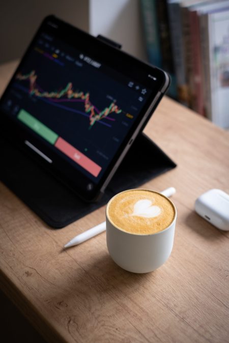 A vertical shot of a tablet device, white mug of a classic nescafe, ear pods and a white pen on a wood table